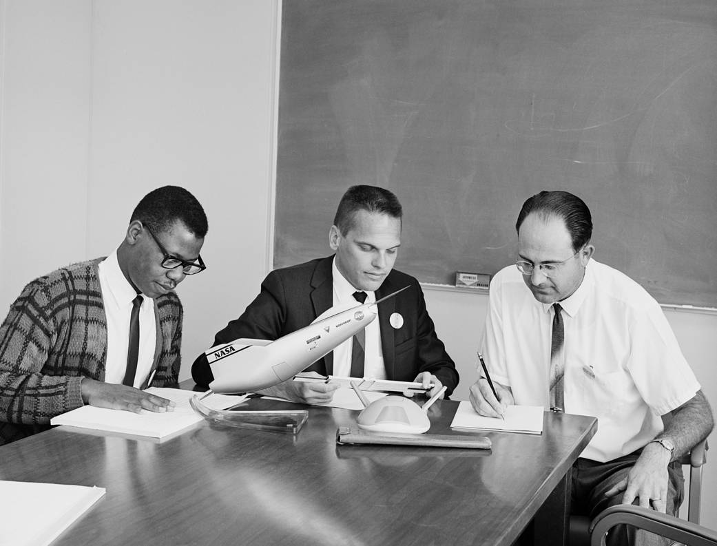 Three men look at aircraft models.