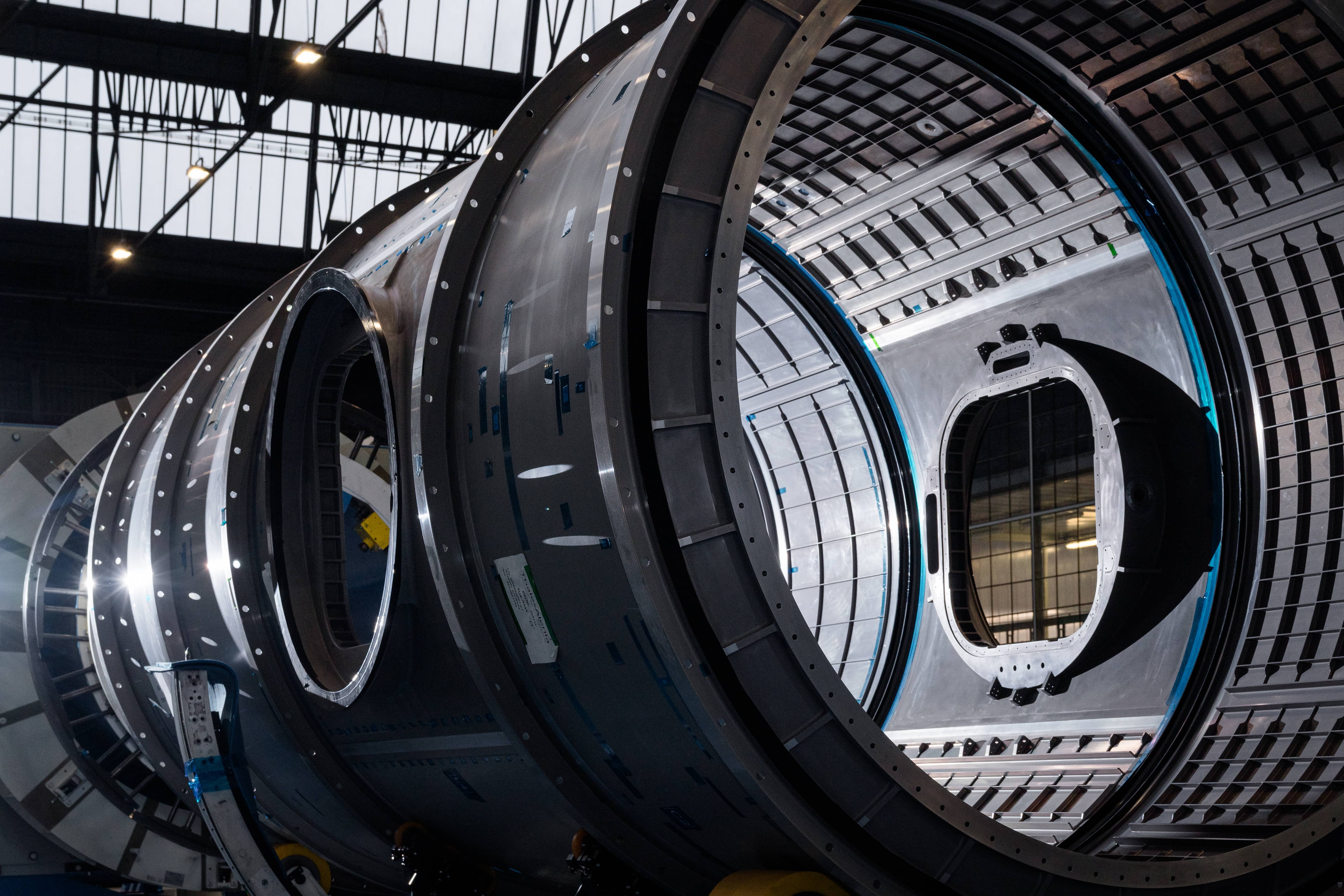 A close-up view of Gateway’s Habitation and Logistics Outpost (HALO) module at the Thales Alenia Space facility in Turin, Italy. The image captures the intricate internal structure of the cylindrical module, highlighting its framework and the interior. The module is positioned horizontally, with light casting dramatic shadows.