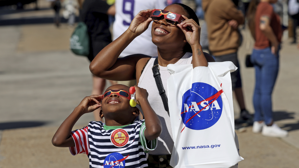 An adult and young child wearing solar eclipse glasses look up