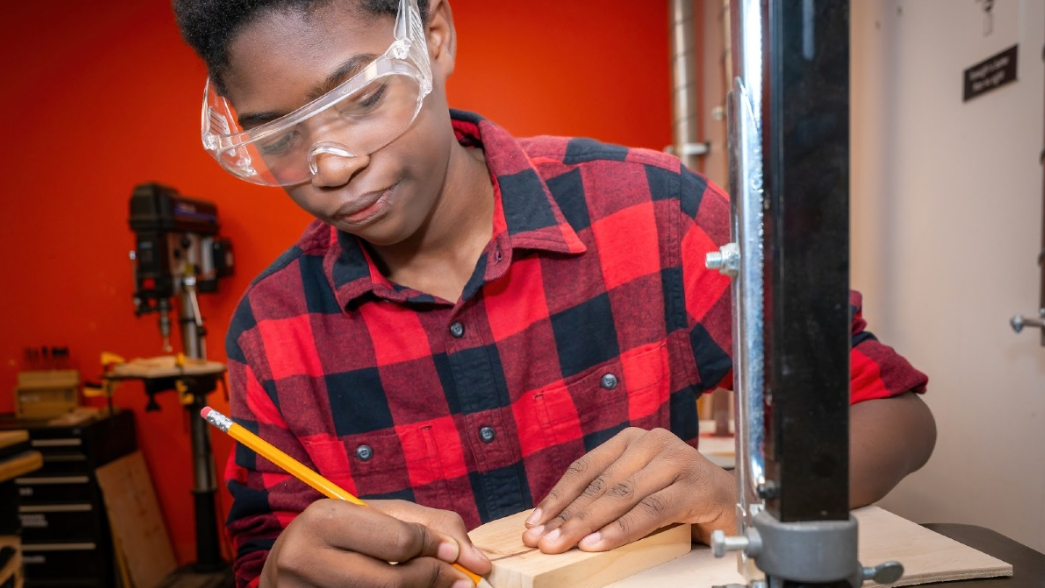 a camp-goer wearing safety goggles as he traces a wood design