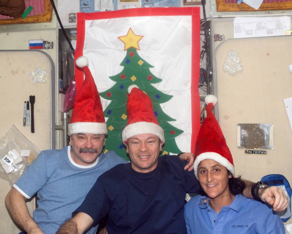 Two men and a woman done blue shirts and Santa hats while serving on Expedition 14 during Christmas 2005