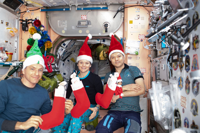 Two men and a woman post in Santa hats and hold Christmas stockings