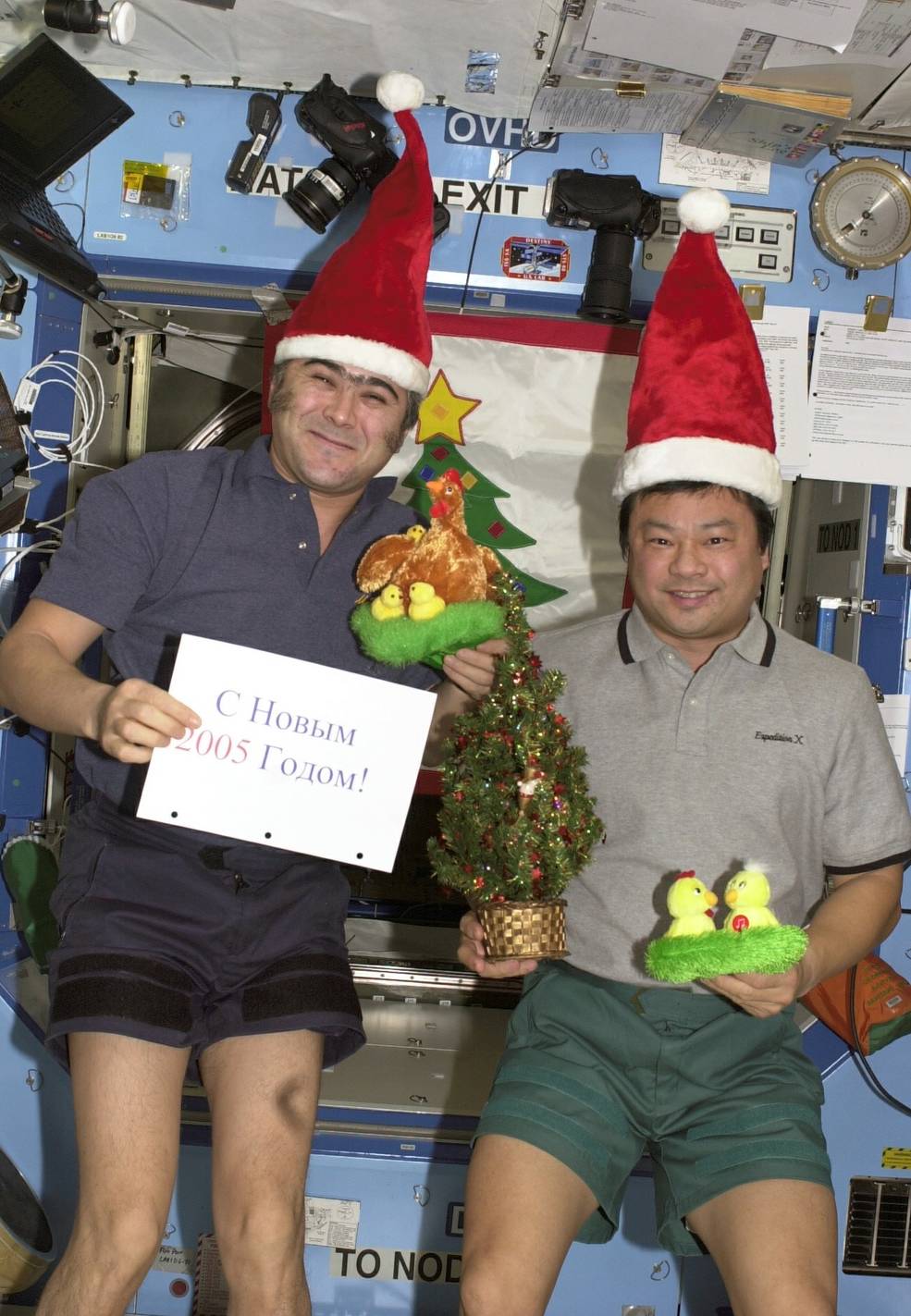 The men in shirts, shorts, and Santa hats hold a sign and other decor while celebrating New Year's Eve