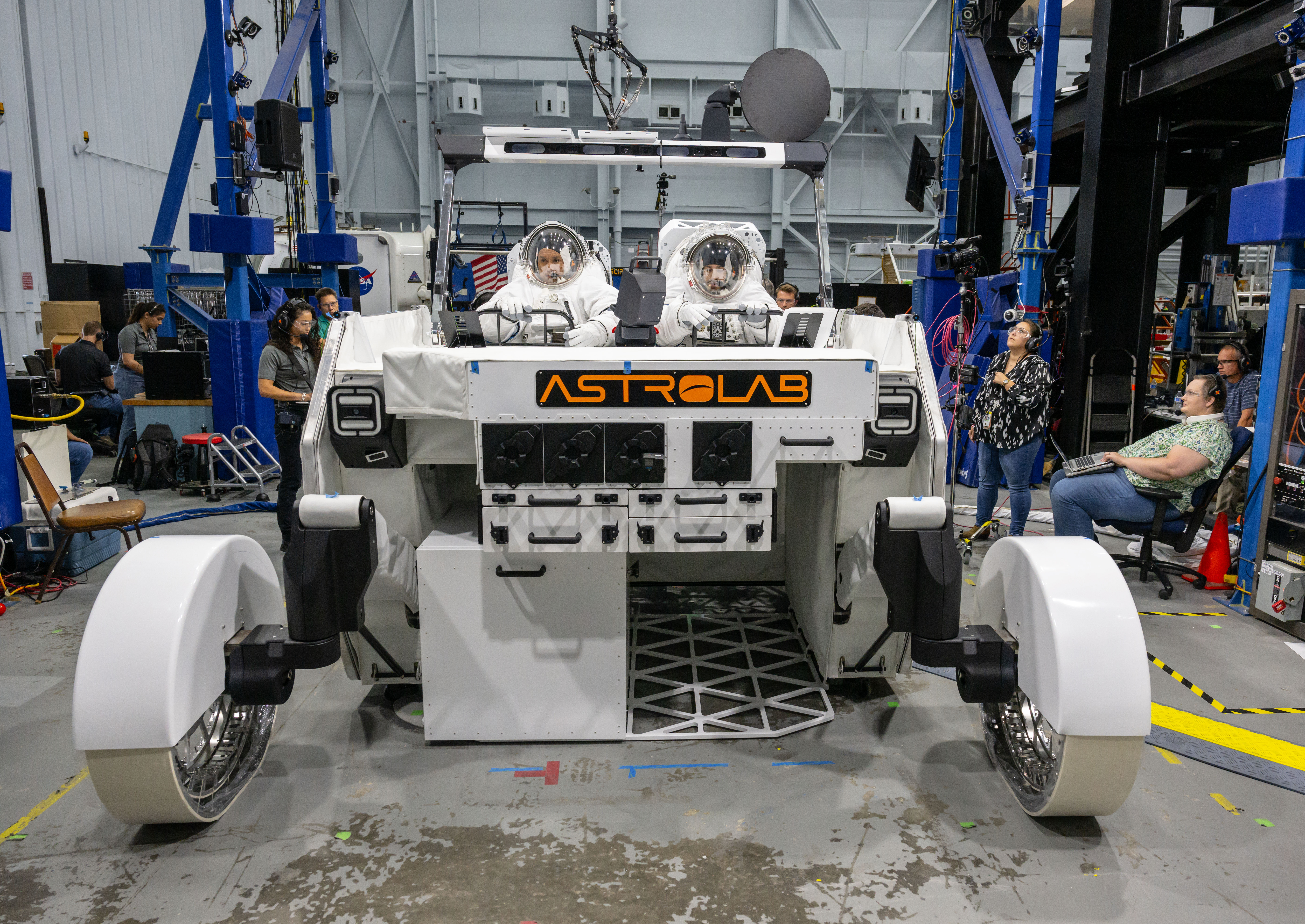 NASA astronaut Frank Rubio and NASA spacesuit engineer Zach Tejral sit inside Astrolab’s FLEX lunar terrain vehicle while wearing white spacesuits. The rover is white with an orange Astrolab logo on the front.