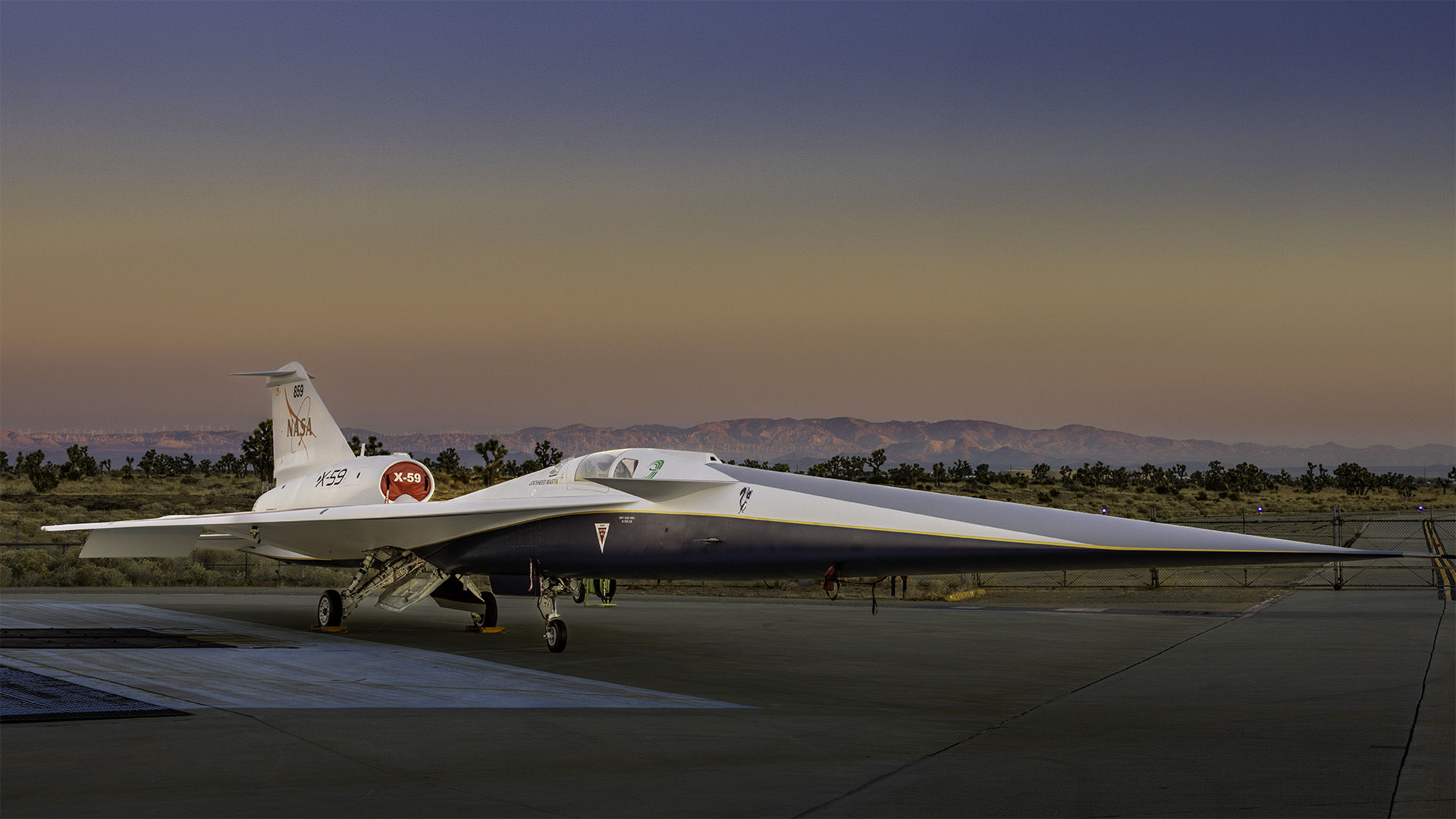 The X-59 sits on a runway with a sunset and moutains in the background.