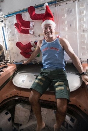 a white man in a tank top pants and Santa hat poses as an elf