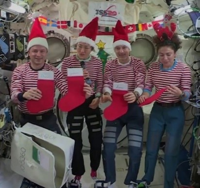 four people in Santa hats and red and white striped shirts hold Christmas stockings