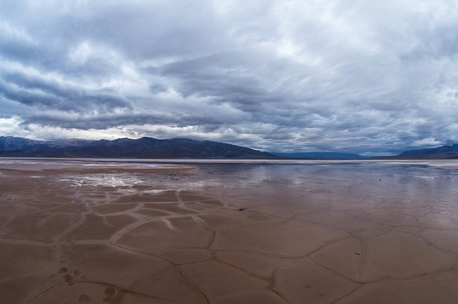 A shallow pool of water over a cracked valley floor underneath a cloudy sky.