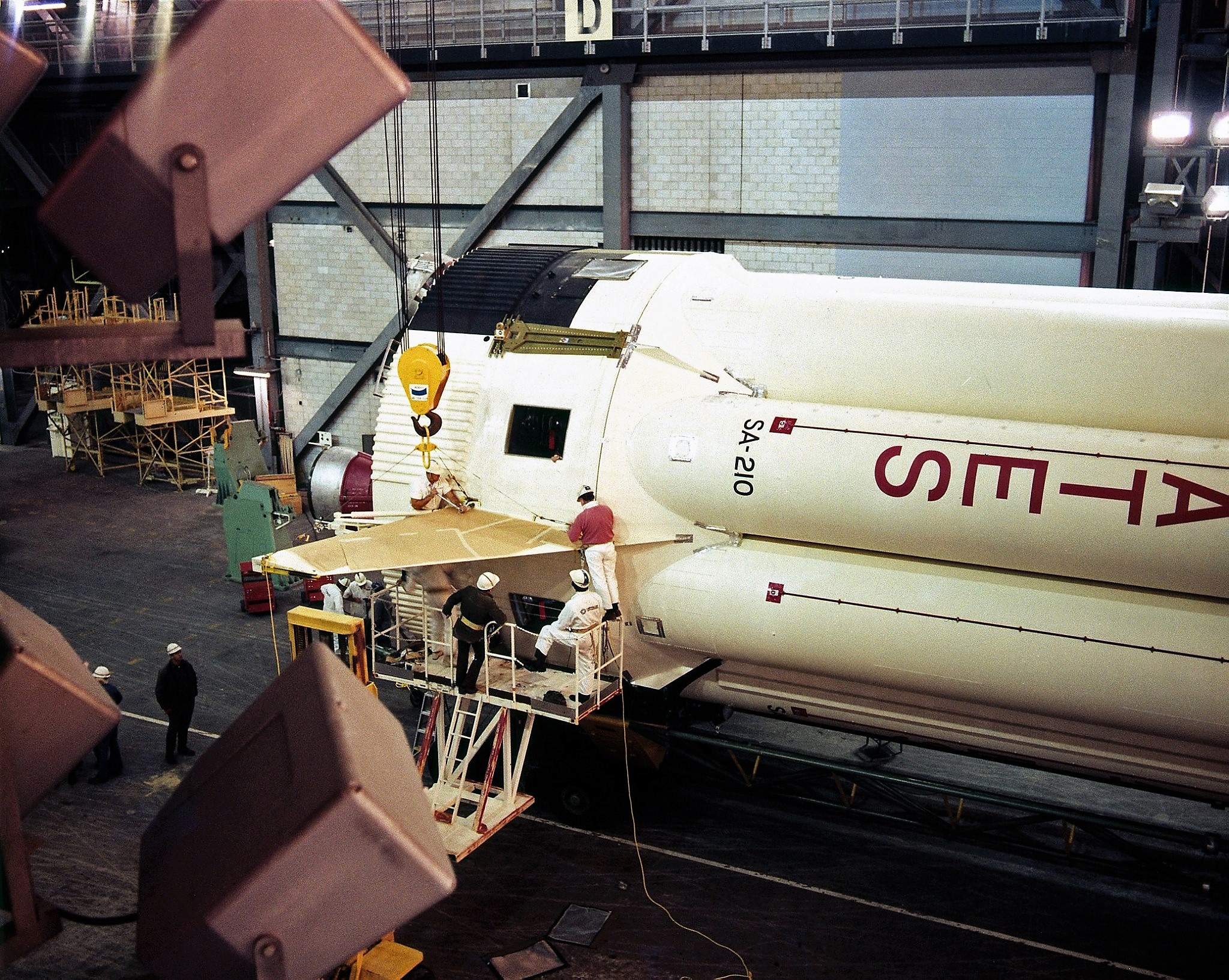 Image of the bottom end of a white rocket stage lying on its side with several workmen working on it.