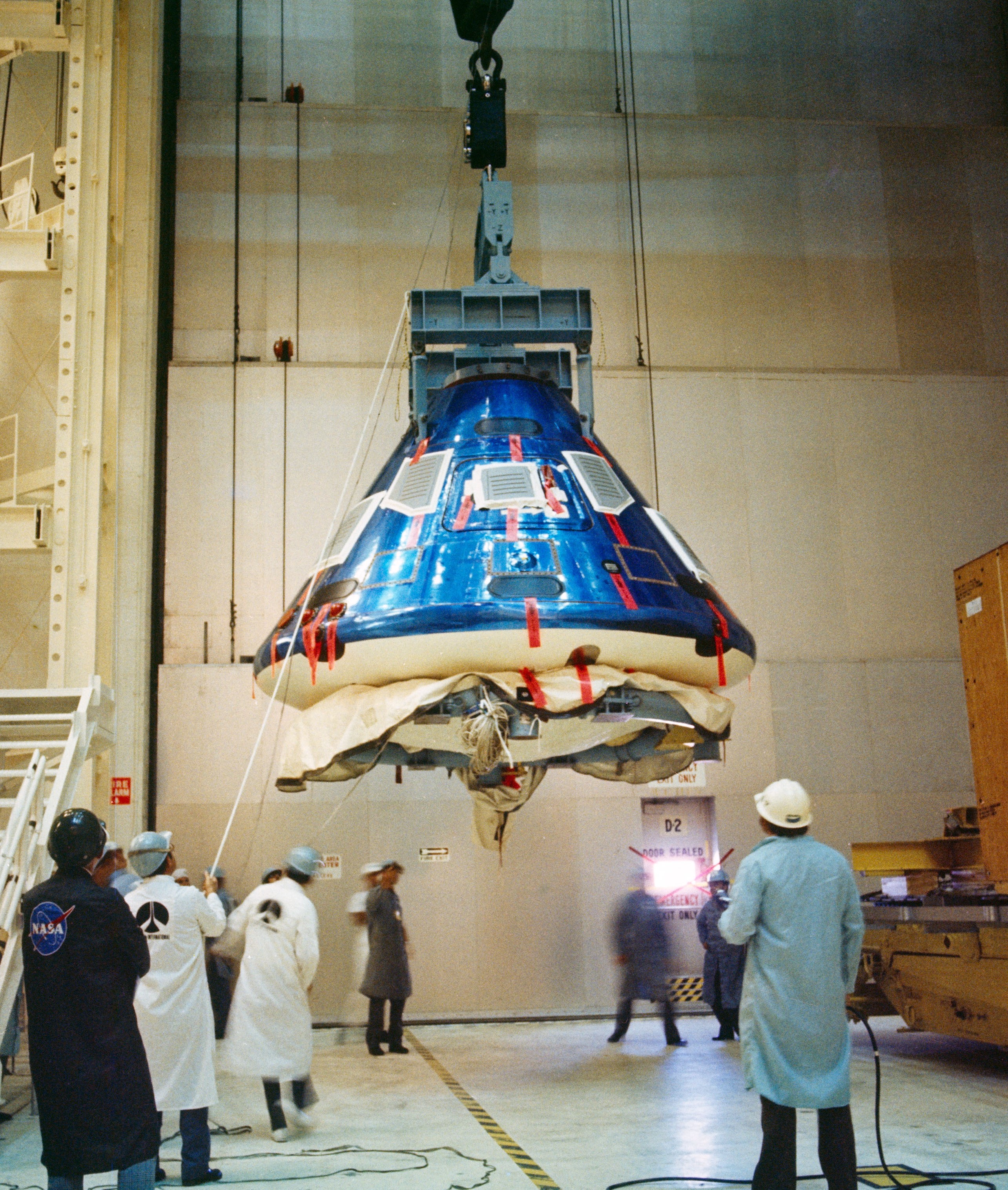 A blue cone-shaped spacecraft hanging from a crane inside a large hanger