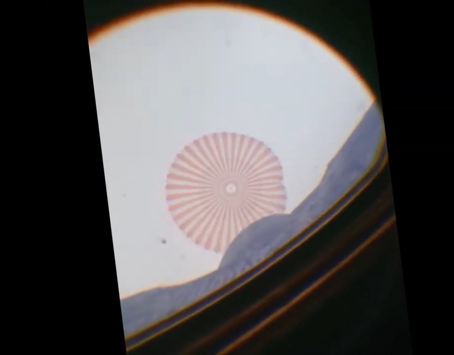 Image taken through a spacecraft window of an open red and white striped parachute.