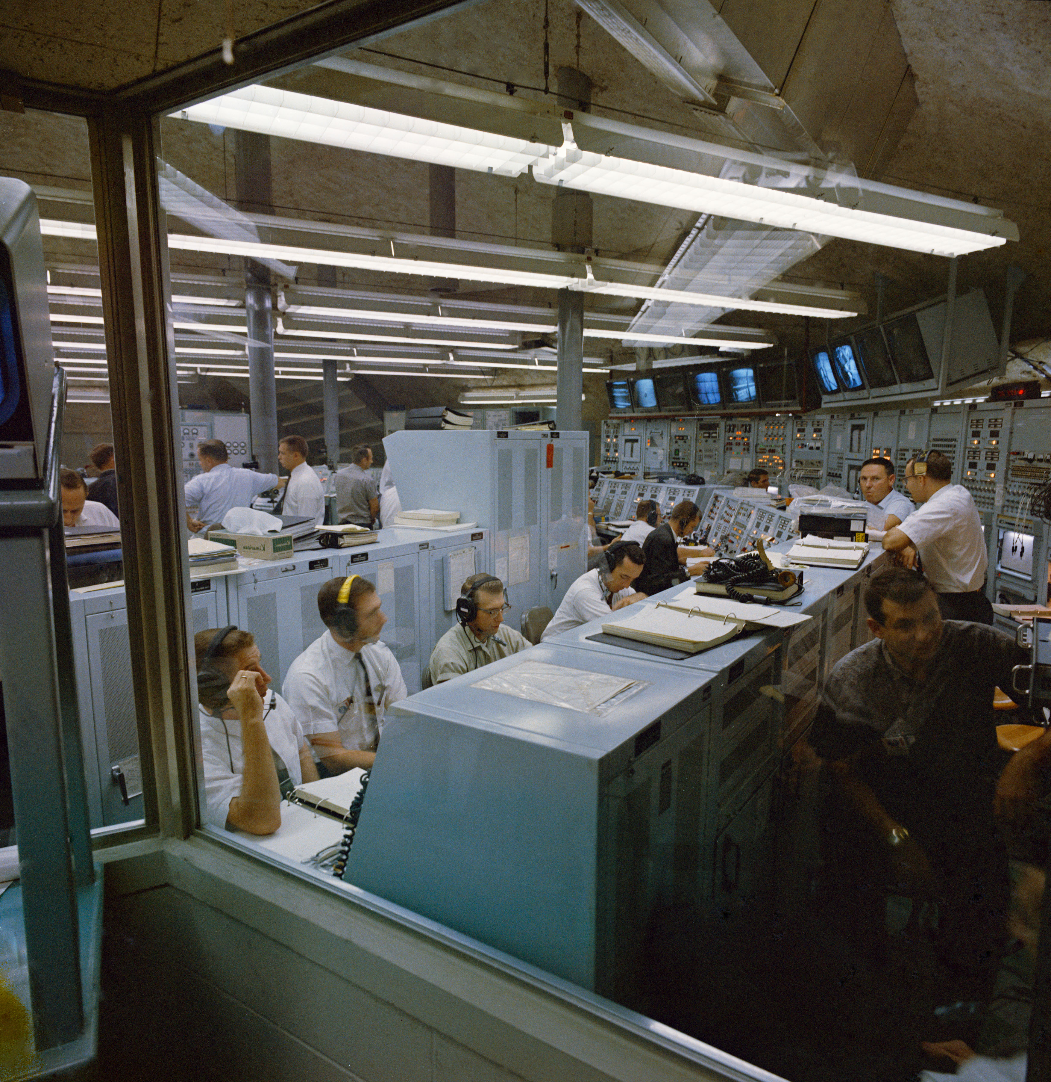 Men in white shirts sitting at consoles in a control room.