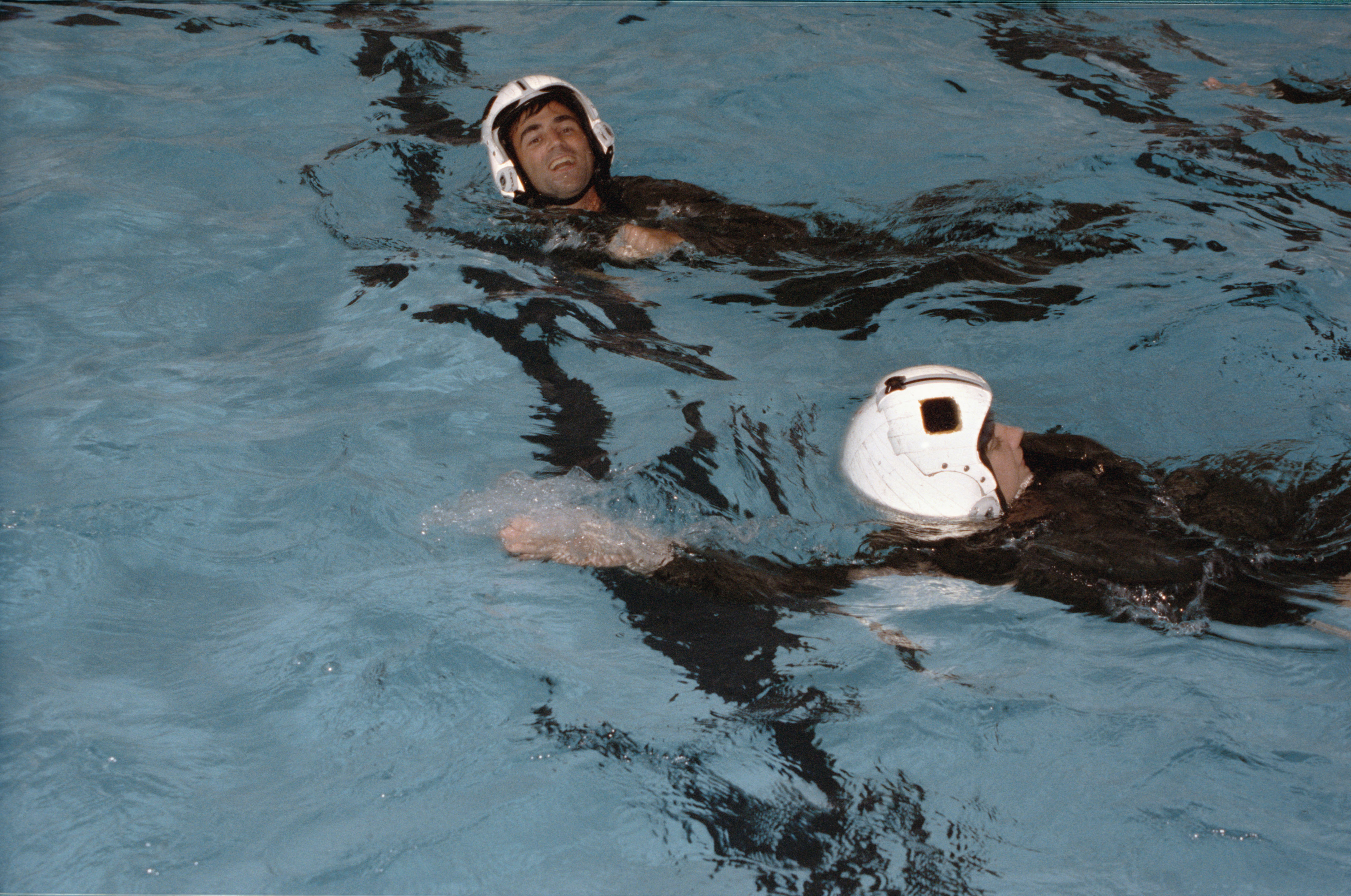 A man and a woman wearing white helmets in a swimming pool