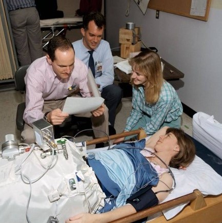 A group of two men and two women in a laboratory setting. One woman is supine and the lower half of her body is inside a white device.